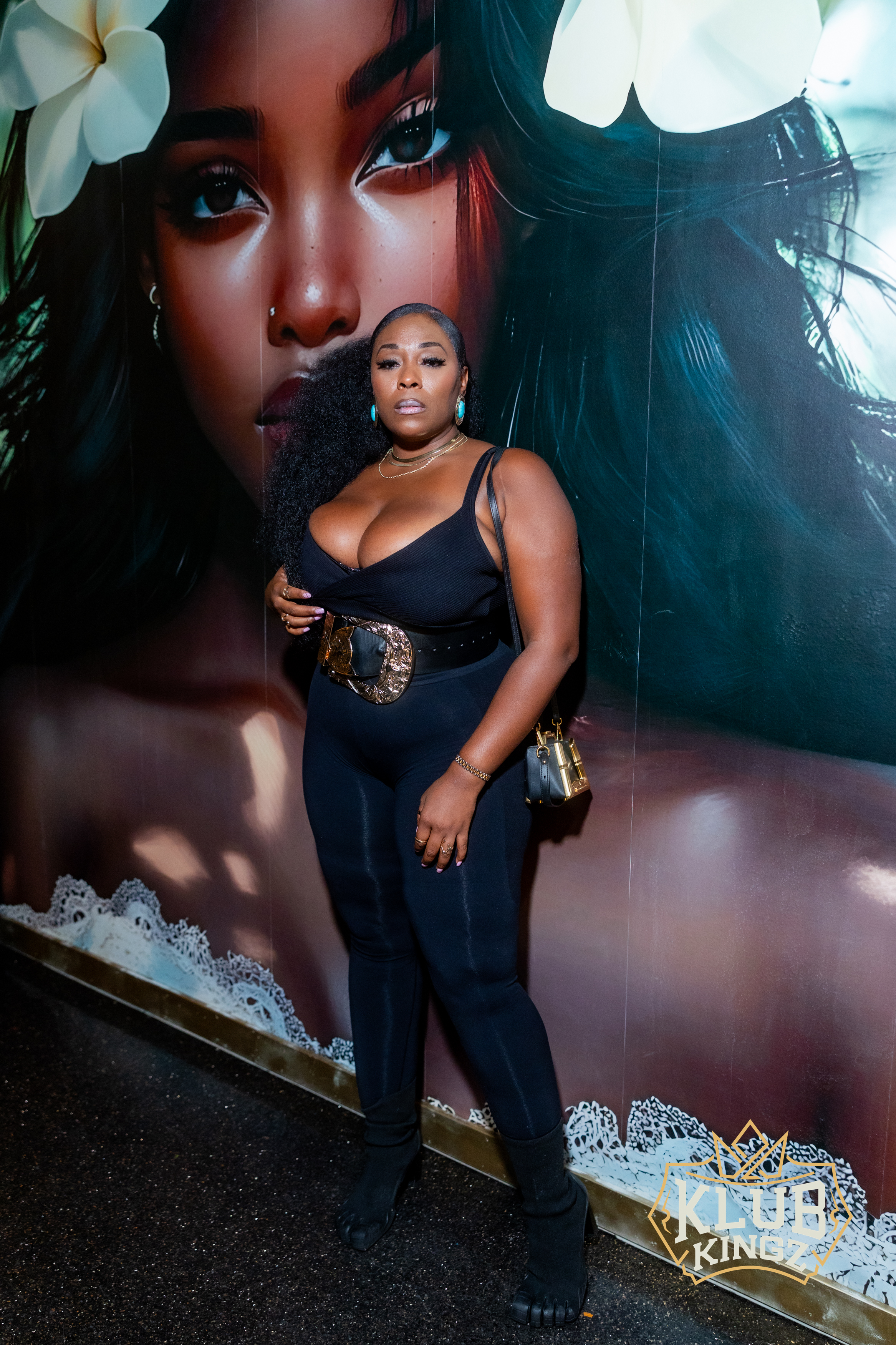 Woman in black outfit with statement belt posing at Klub Kingz nightlife event mural