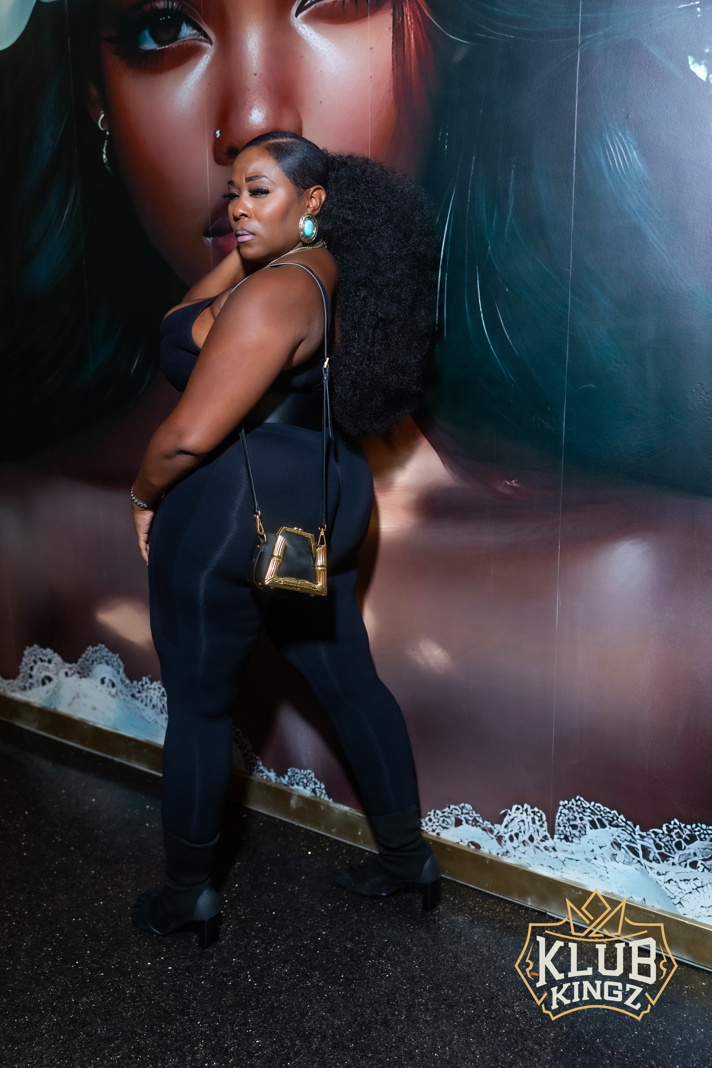 Woman in black bodysuit poses beside mural artwork at Klub Kingz nightlife event