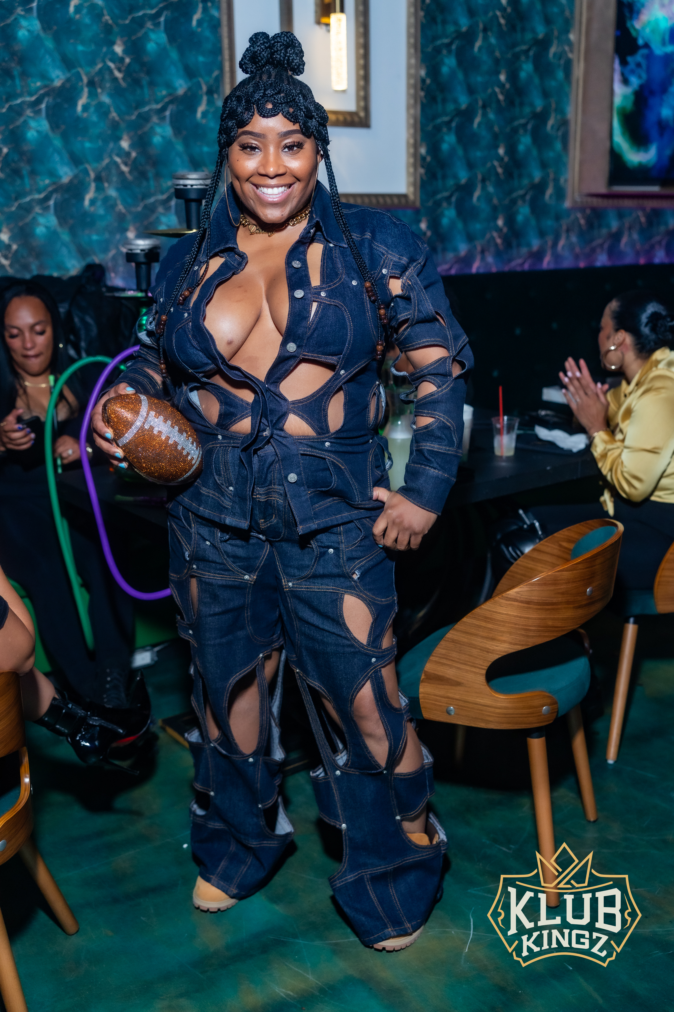 Woman in cutout denim outfit holding rhinestone football at Klub Kingz nightlife event