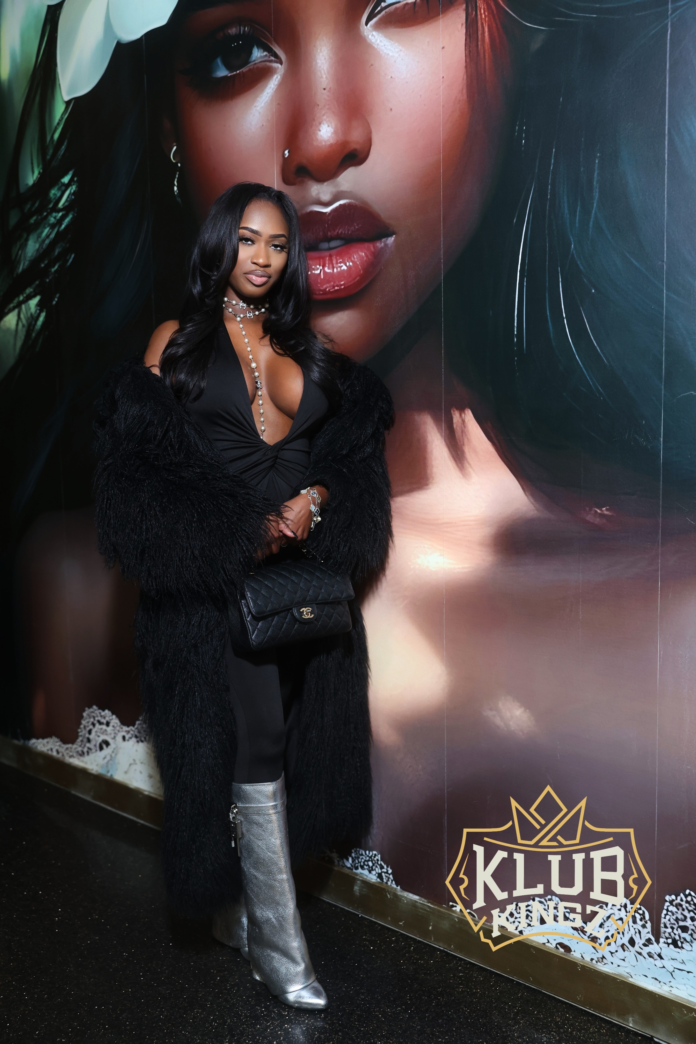 Stylish woman in black fur coat poses by Klub Kingz mural wall for nightlife event photo
