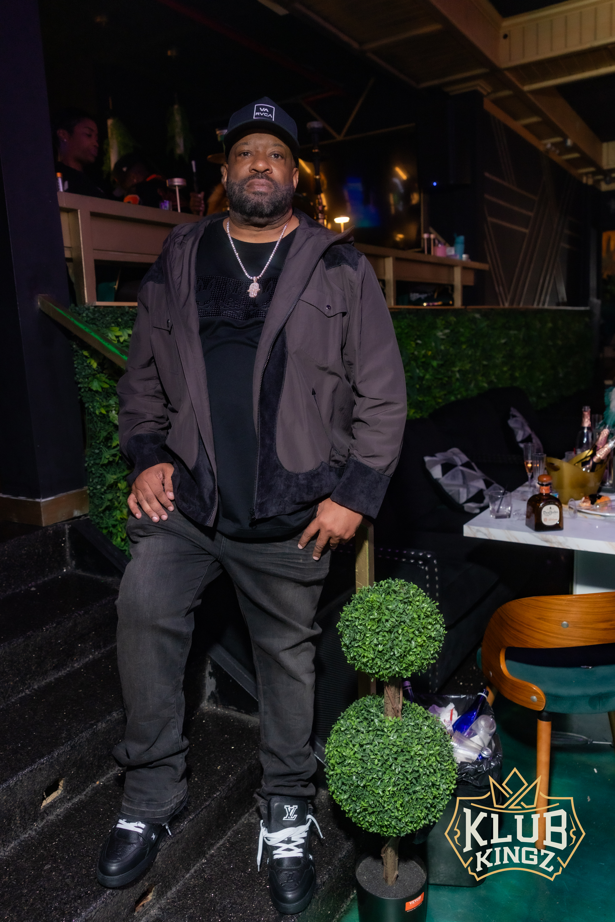 Man in cap and brown jacket posing on stairs at Klub Kingz nightclub event