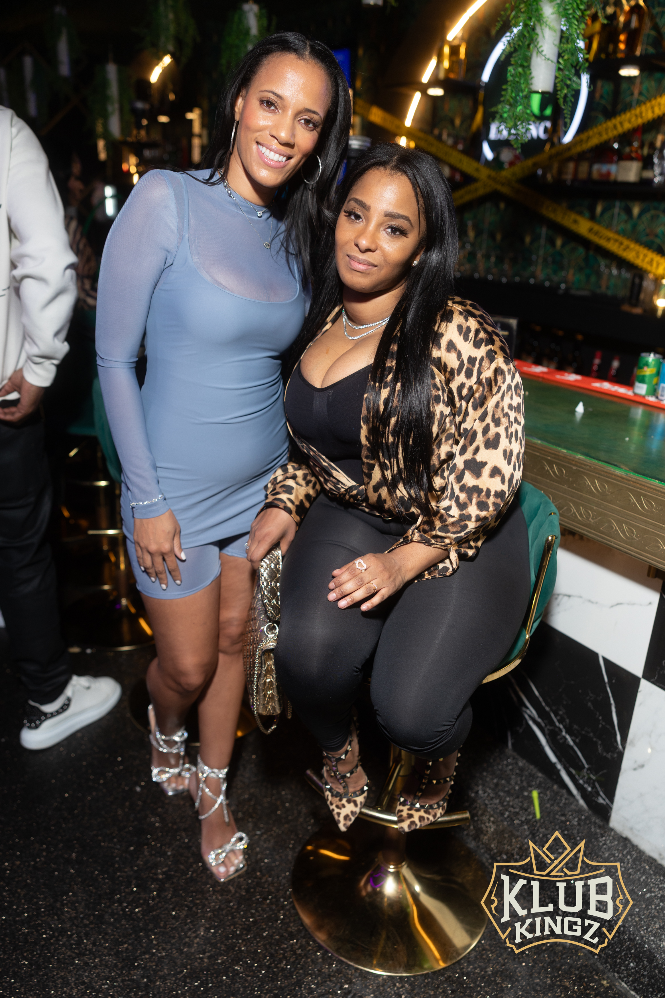 Two stylish women posing together at the bar during a Klub Kingz nightlife event