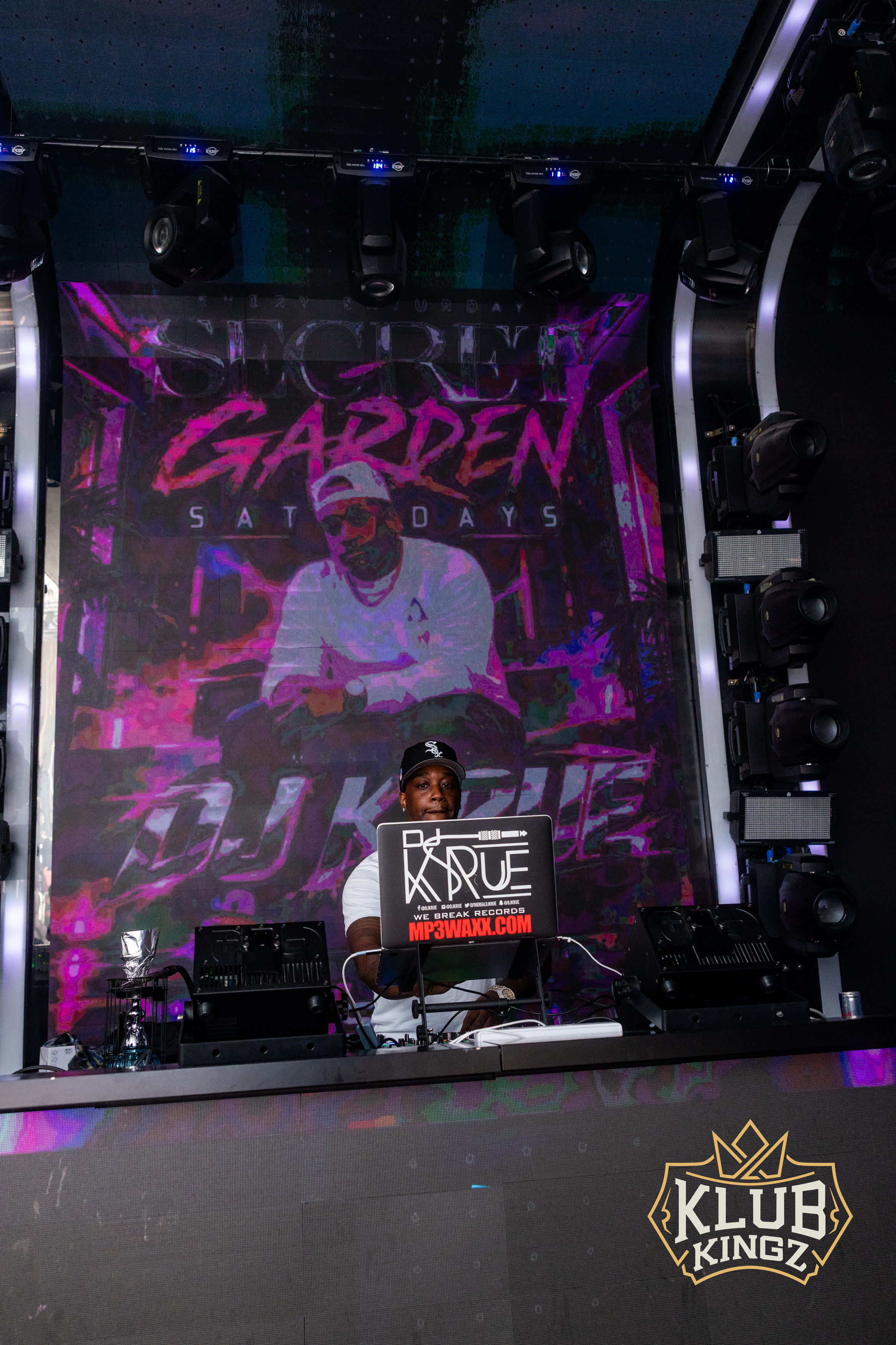 DJ performing at Klub Kingz for Secret Garden Saturdays, colorful stage backdrop and lighting rig.