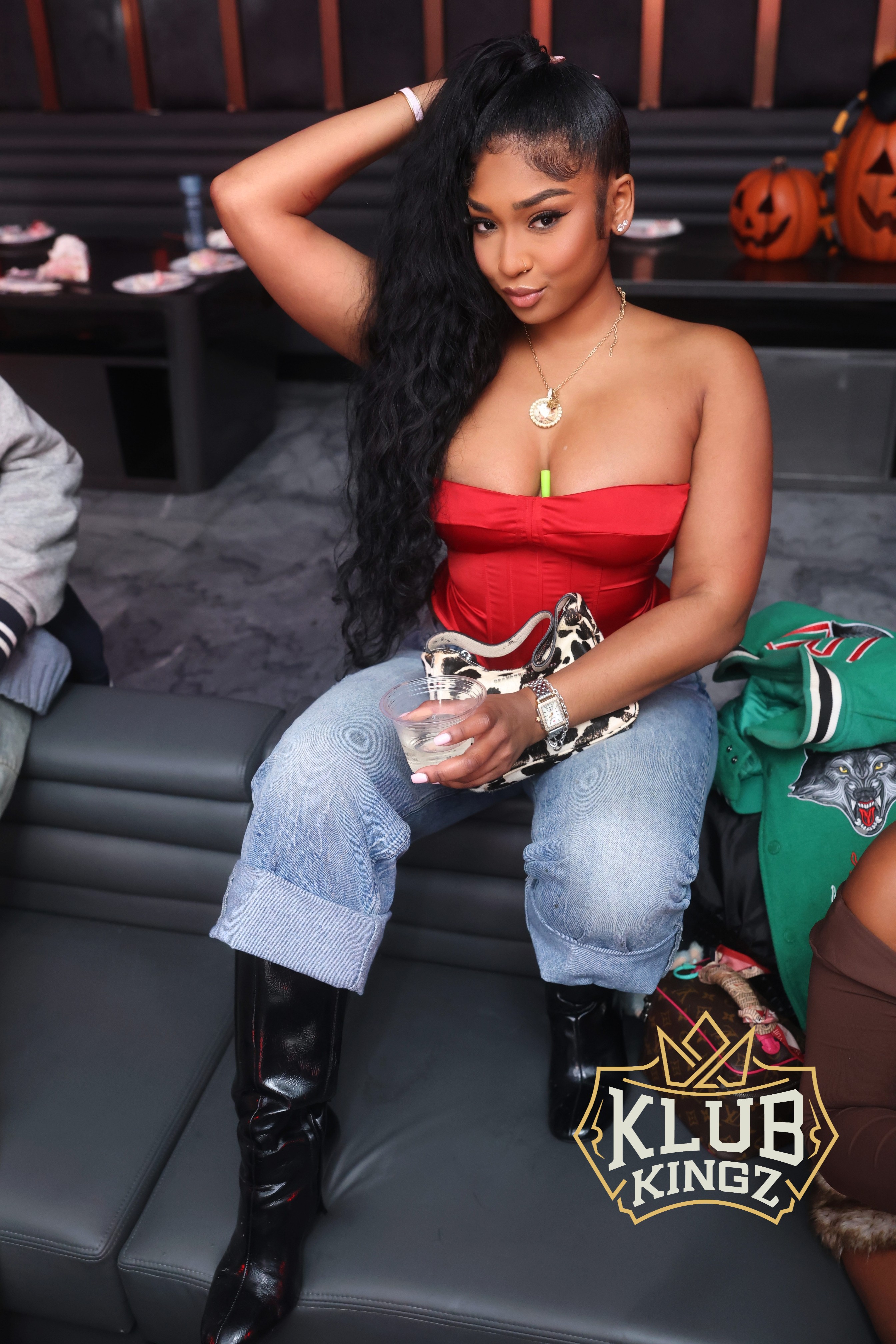 Woman in red top and jeans posing with drink on VIP booth seating at Klub Kingz nightlife event