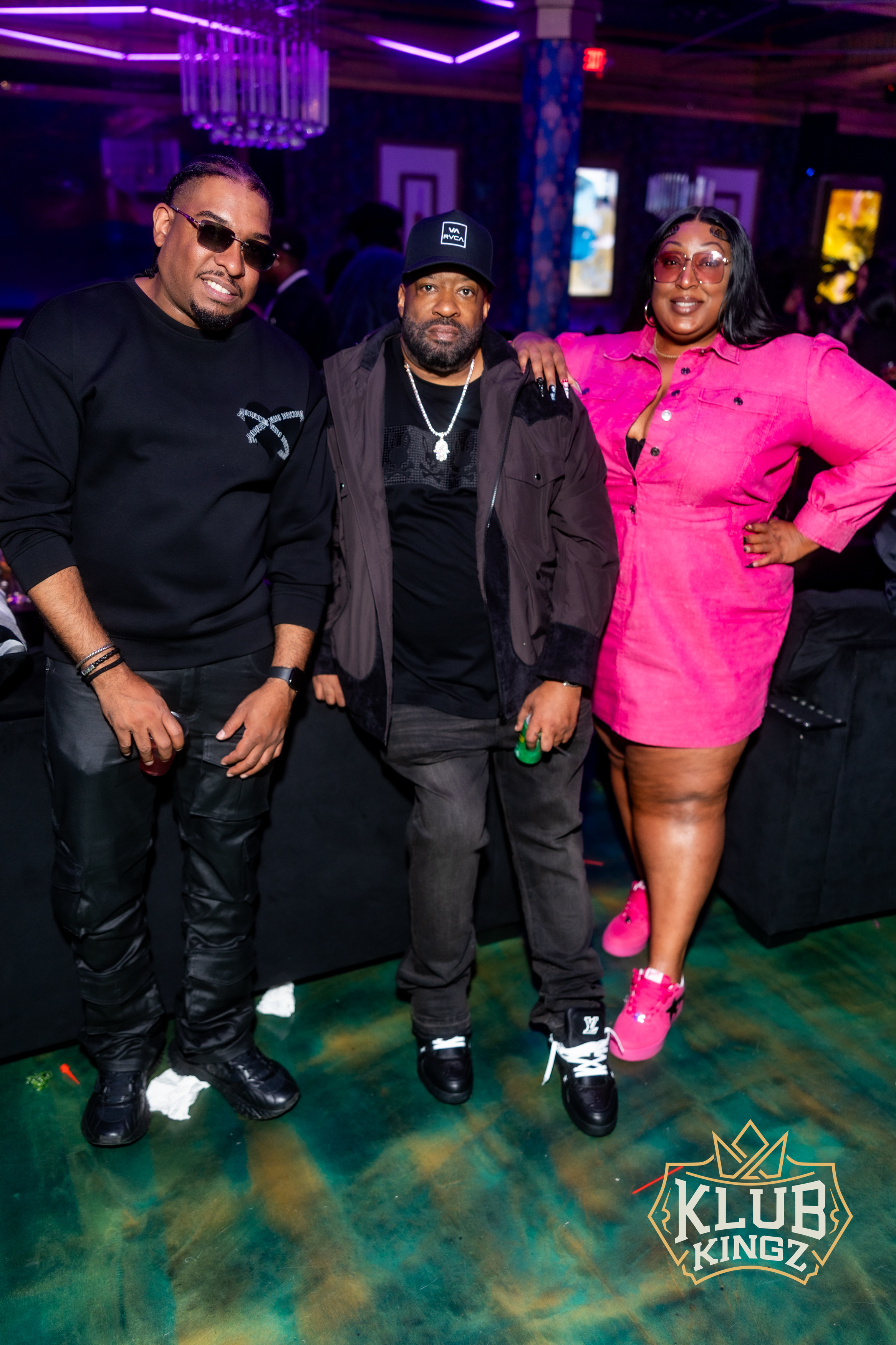 Three friends posing together at Klub Kingz nightclub, stylish outfits and vibrant lighting.