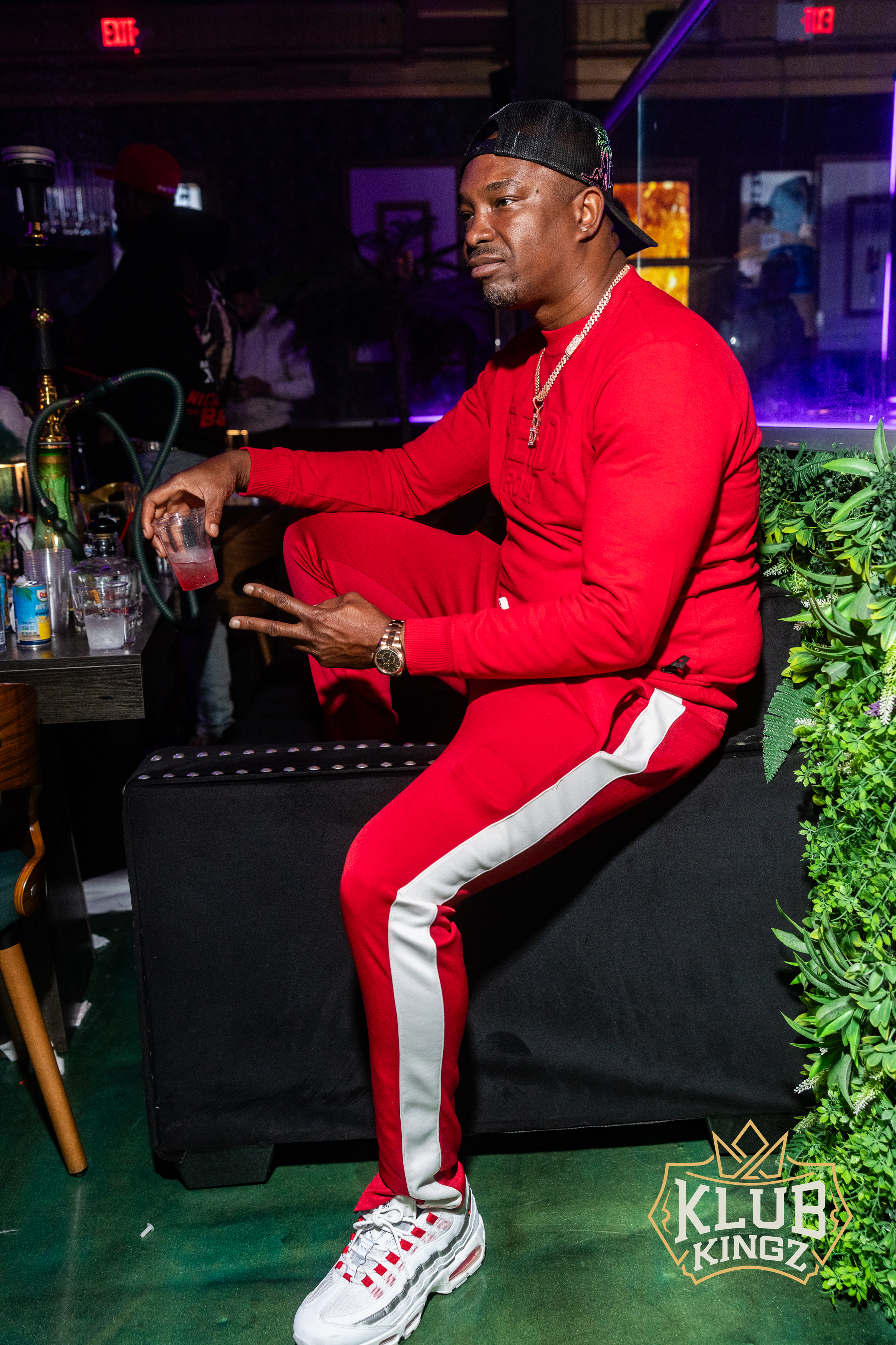 Man in red tracksuit and backwards cap holding a drink at Klub Kingz nightclub lounge