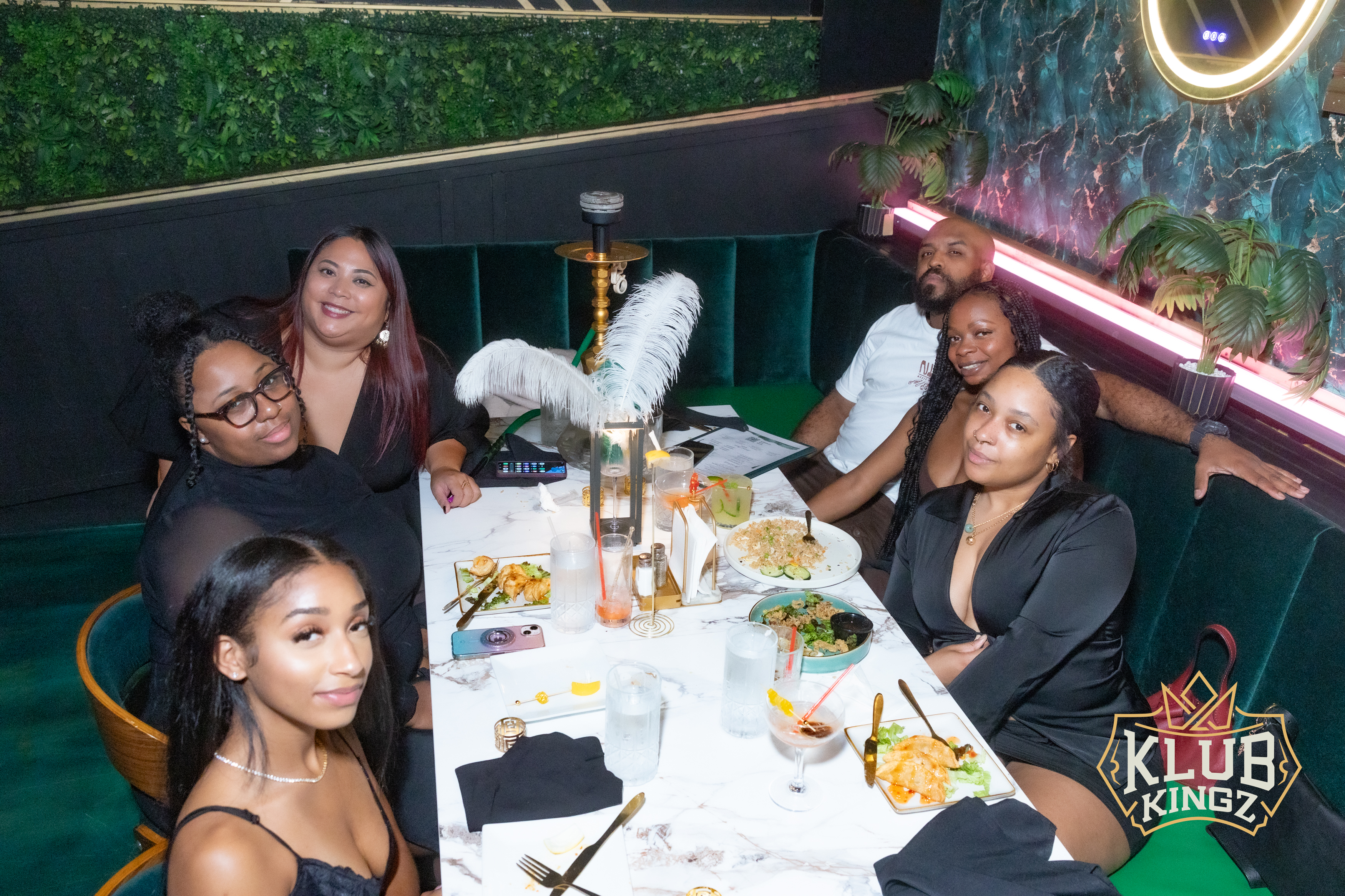 Friends enjoying dinner, cocktails, and hookah at Klub Kingz lounge with lush green booth seating