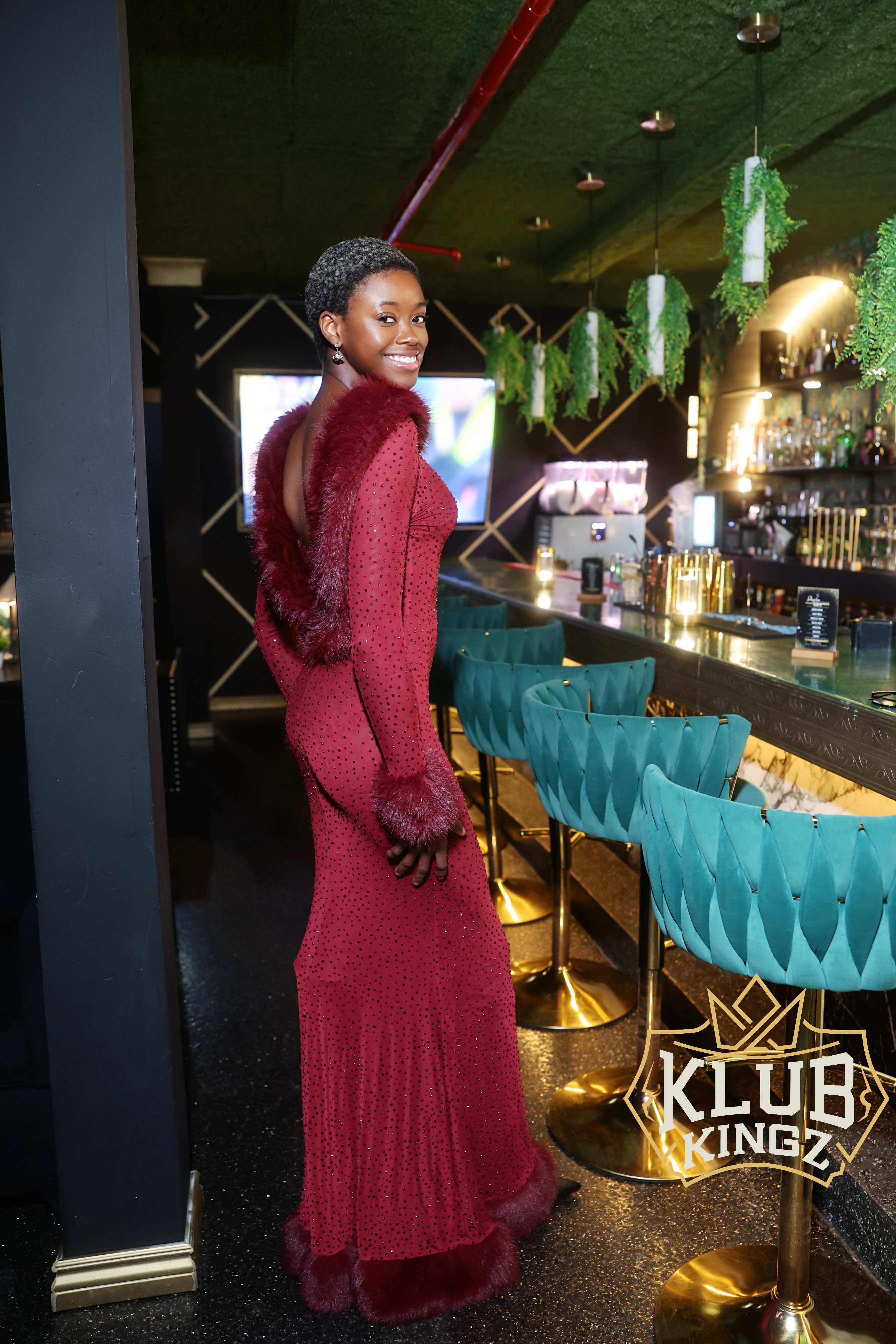 Woman in red fur-trimmed gown posing by the bar at Klub Kingz nightclub