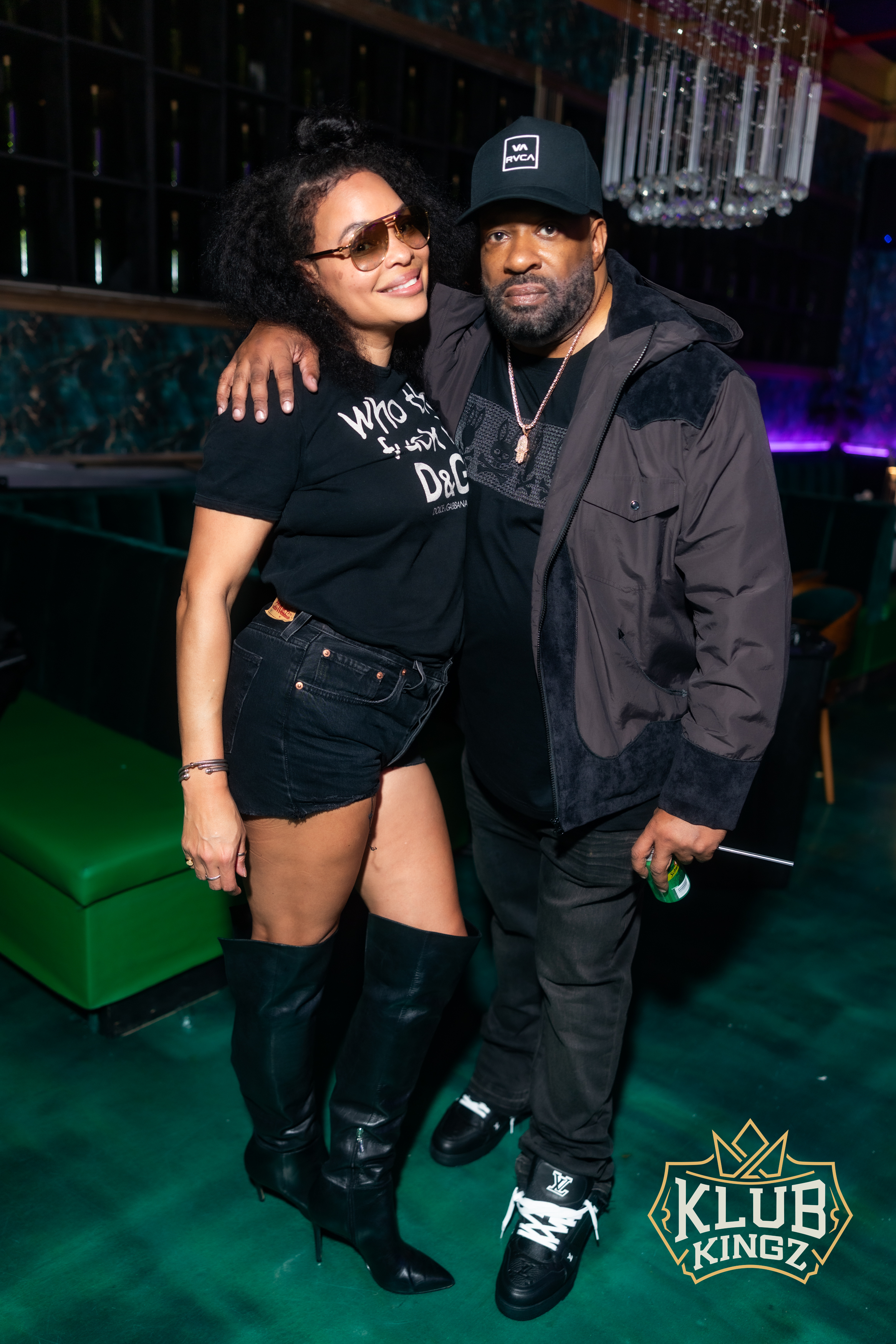 Couple posing together at Klub Kingz nightclub, dressed in stylish black outfits under chandelier lighting