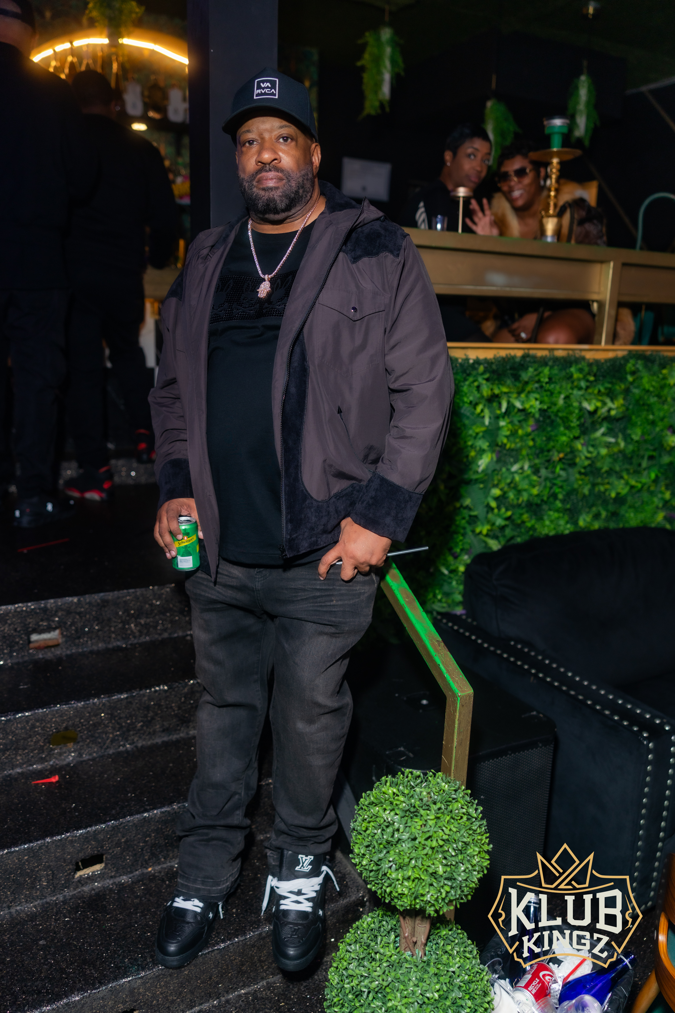 Man in cap and jacket poses on stairs at Klub Kingz nightlife event with hookah lounge seating