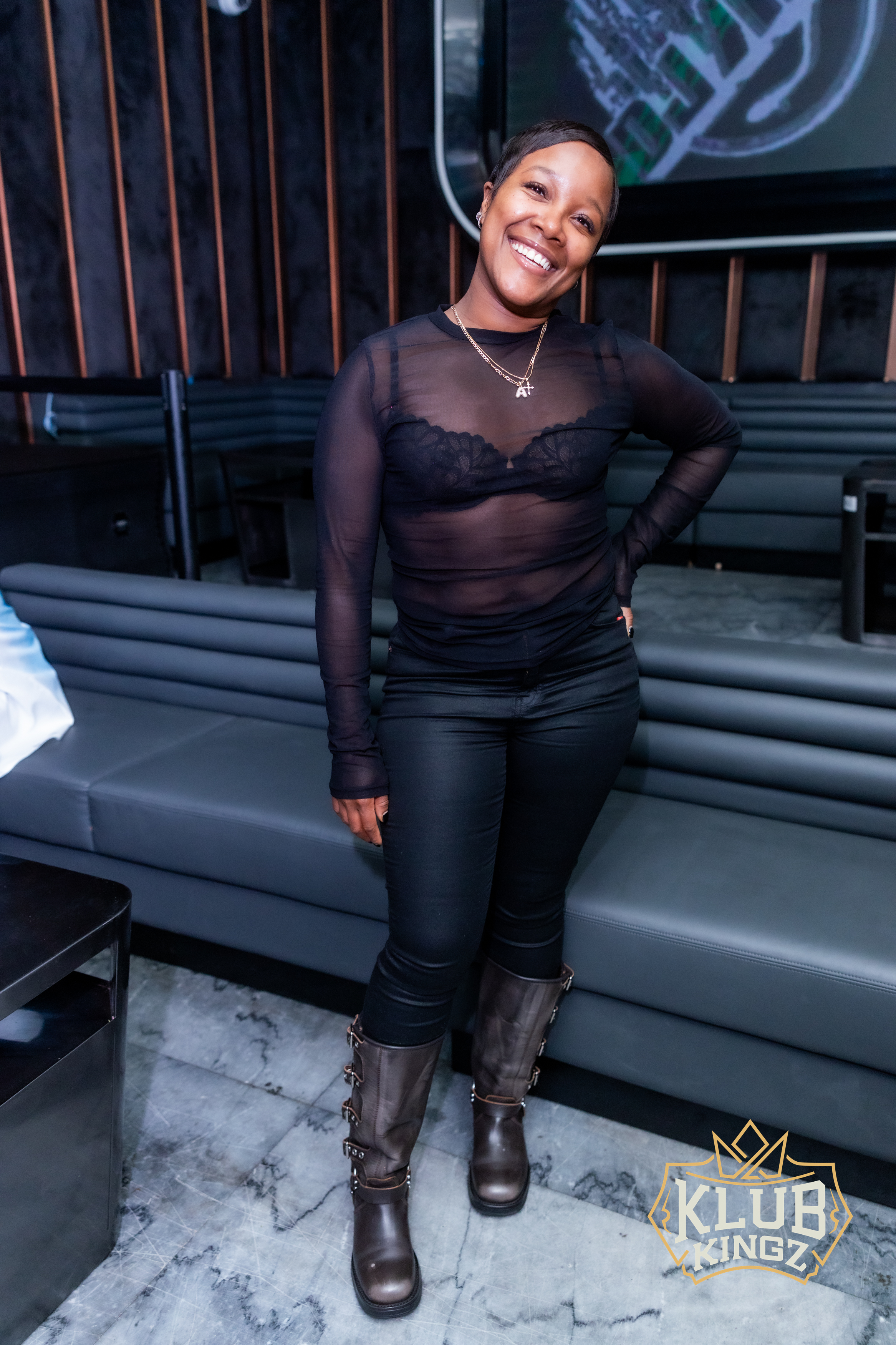 Smiling woman in black outfit and boots posing at Klub Kingz nightclub lounge